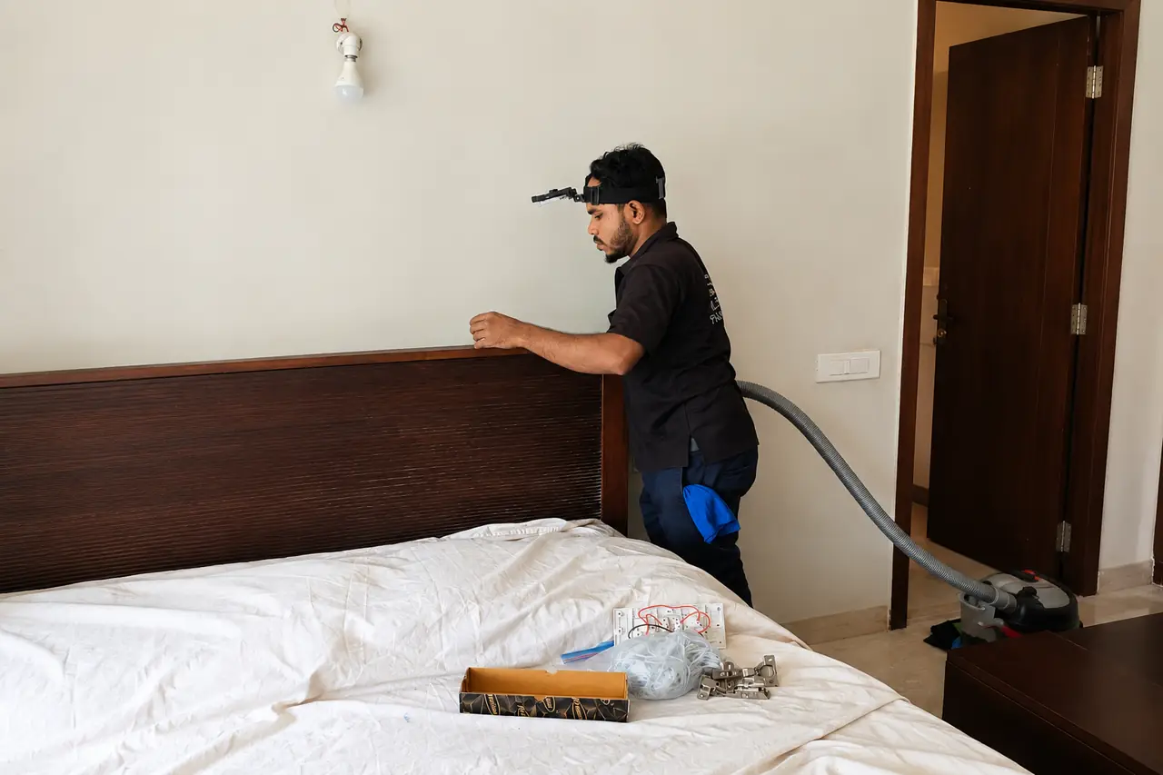 Operator in a head-mounted camera vacuuming behind a bedroom headboard